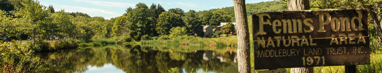 An outdoor shot of a pond with a sign that reads: Fenn's Pond, Natural Area, Middlebury Land Trust, Inc. 1971