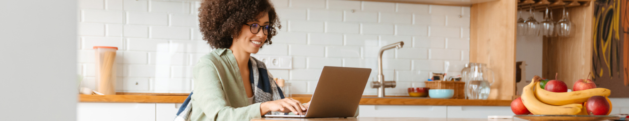 A woman using her laptop and smiling in her kitchen