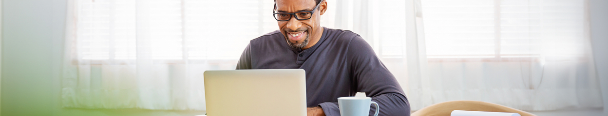 A smiling man wearing glasses and using a laptop inside his home