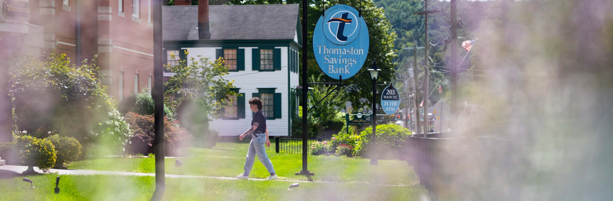 Customer walking on sidewalk towards Thomaston Savings Bank branch on a sunny day