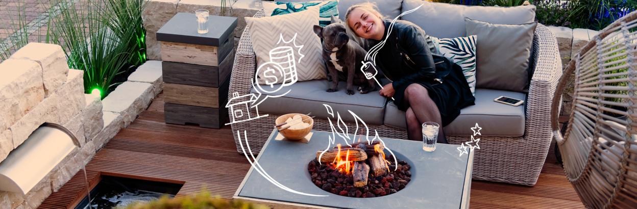 A young woman sitting outside on patio deck with French bulldog near a fire pit