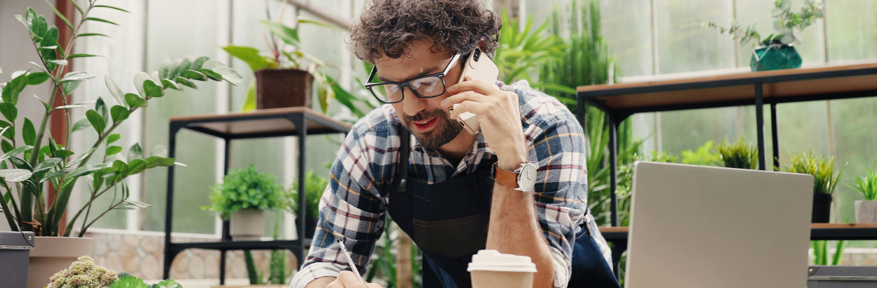 Man wearing glasses talking on cell phone in room filled with greenery