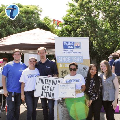 Thomaston Savings Bank employees hold a sign displaying their contribution to the Stock the Pantry event with canopy tents in the background.