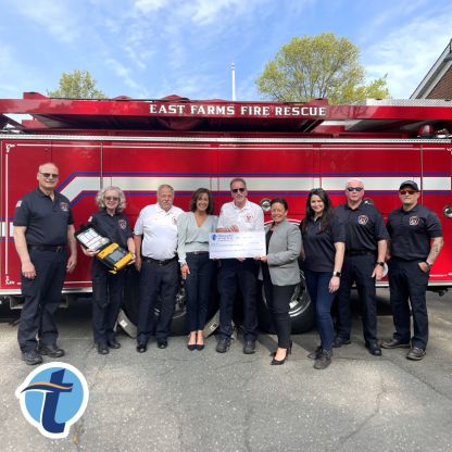 East Farmington Volunteer Fire Department personnel and Thomaston Savings Bank executives hold a big check in front of a fire truck.