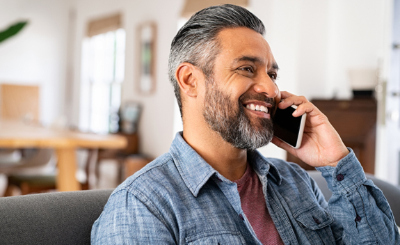 Smiling, middle aged man talking on cell phone while sitting on couch in home