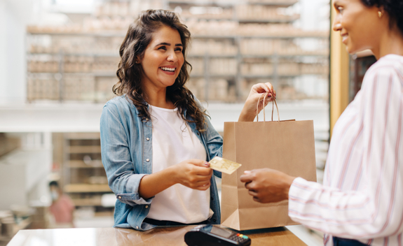 Woman smiling and handing debit card to cashier to pay for merchandise in store