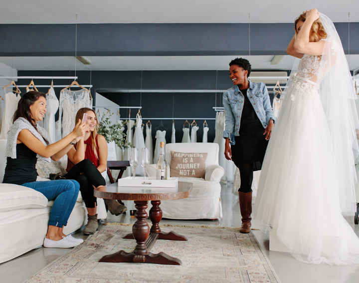 A happy bride trying on a wedding dress in a boutique while her friends watch and take pictures